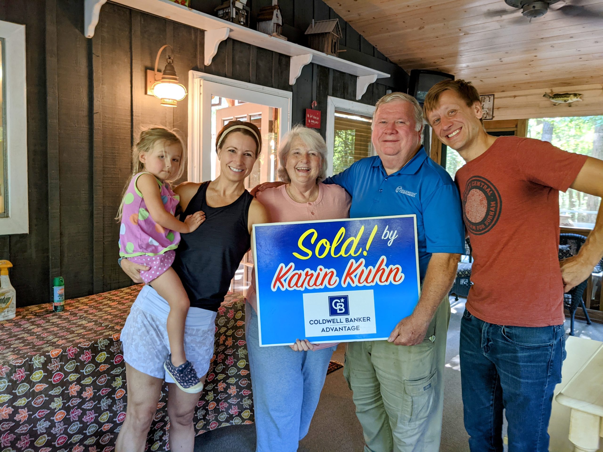 Happy family poses with a "Sold!" sign held by a real estate agent in Virginia, celebrating a successful home sale.
